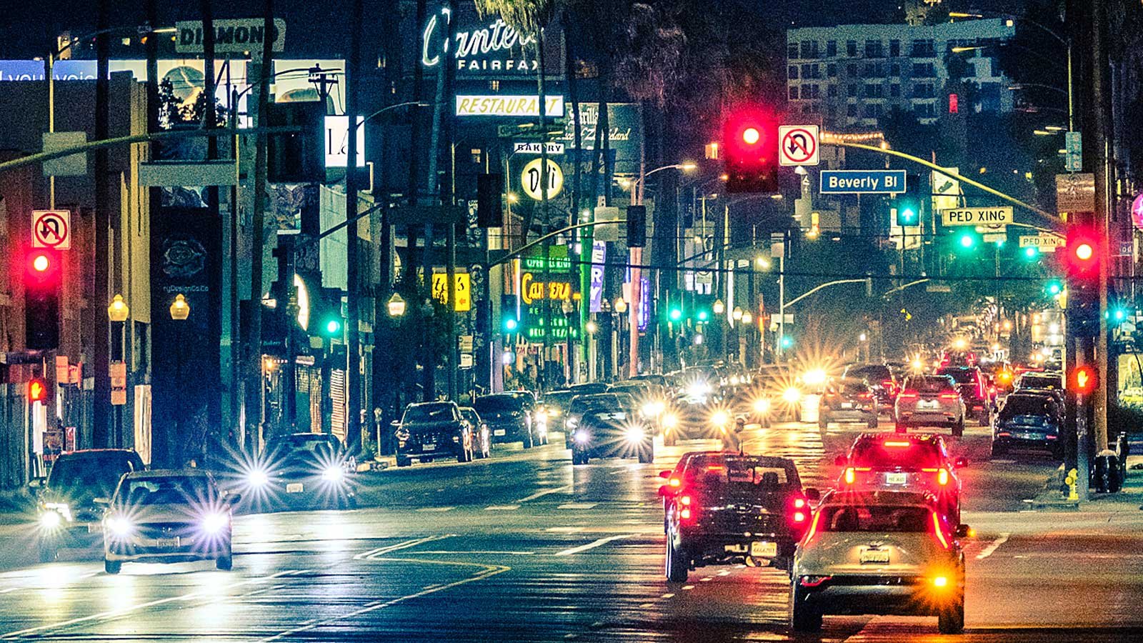 A car head and brake lights shimmer on a busy street on the westside of Los Angeles at night.