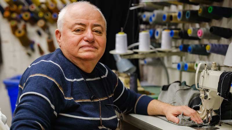 Owner of Gary's Custom Tailoring standing in his shop with a tape measure around his neck.