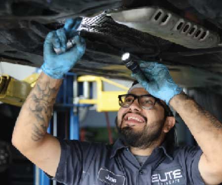 A mechanic working below an automobile at Elite Auto Care.
