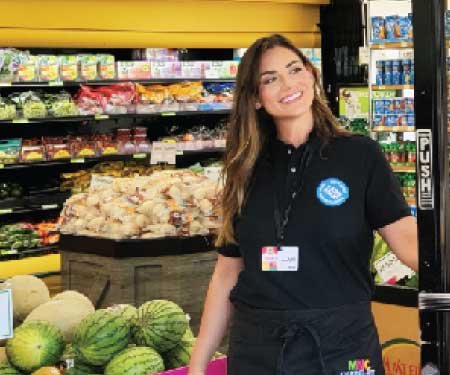 An owner of Mothers Nutritional Center standing in front of fresh fruits and vegetables.