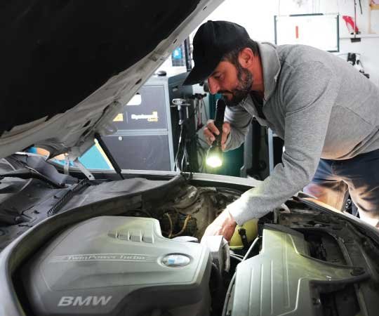A mechanic working under a car's hood at Van Nuys Smog.