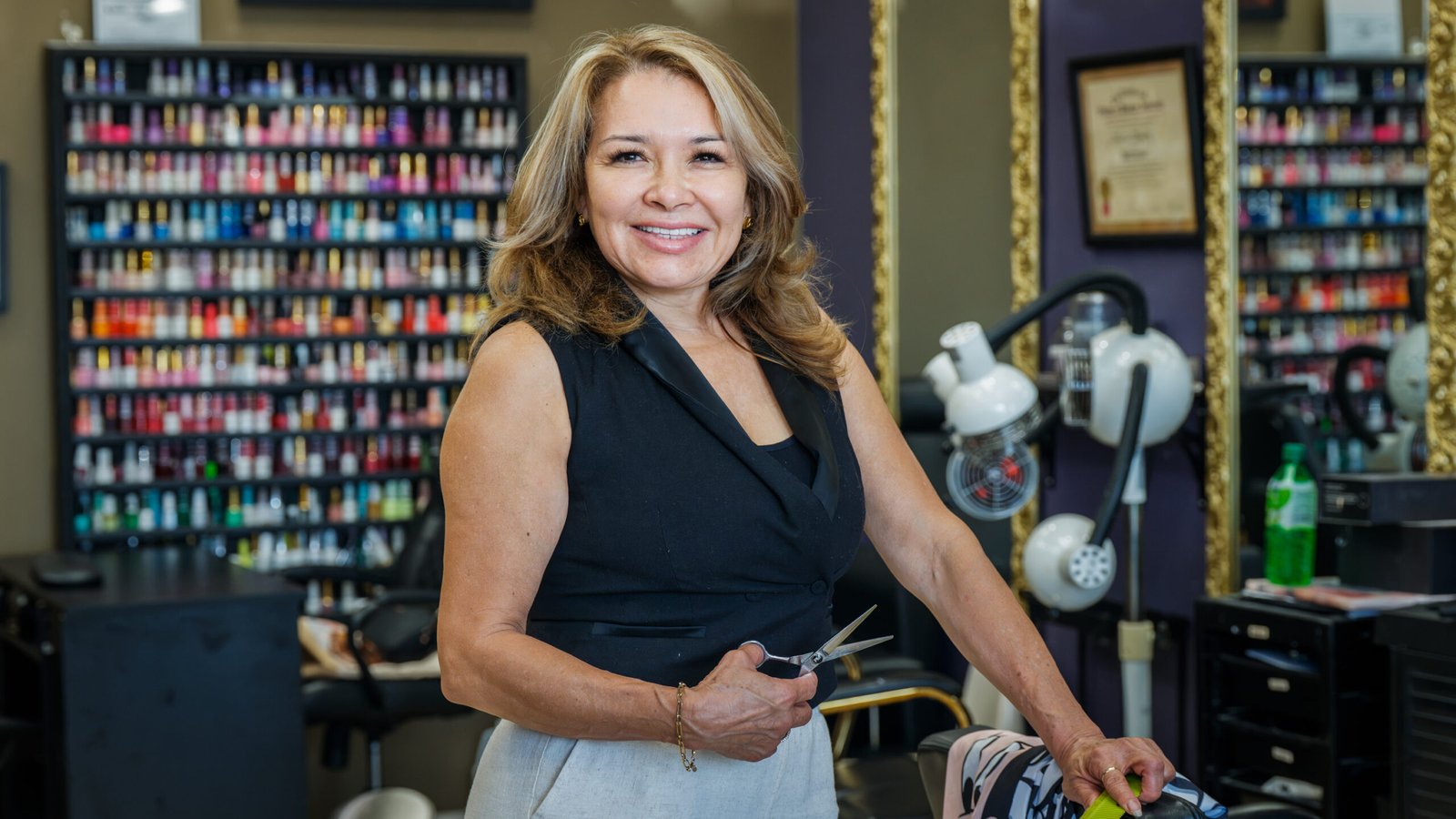 Adi's Beauty Salon – stylist holding scissors in front of a wall of colorful nail polish bottles.