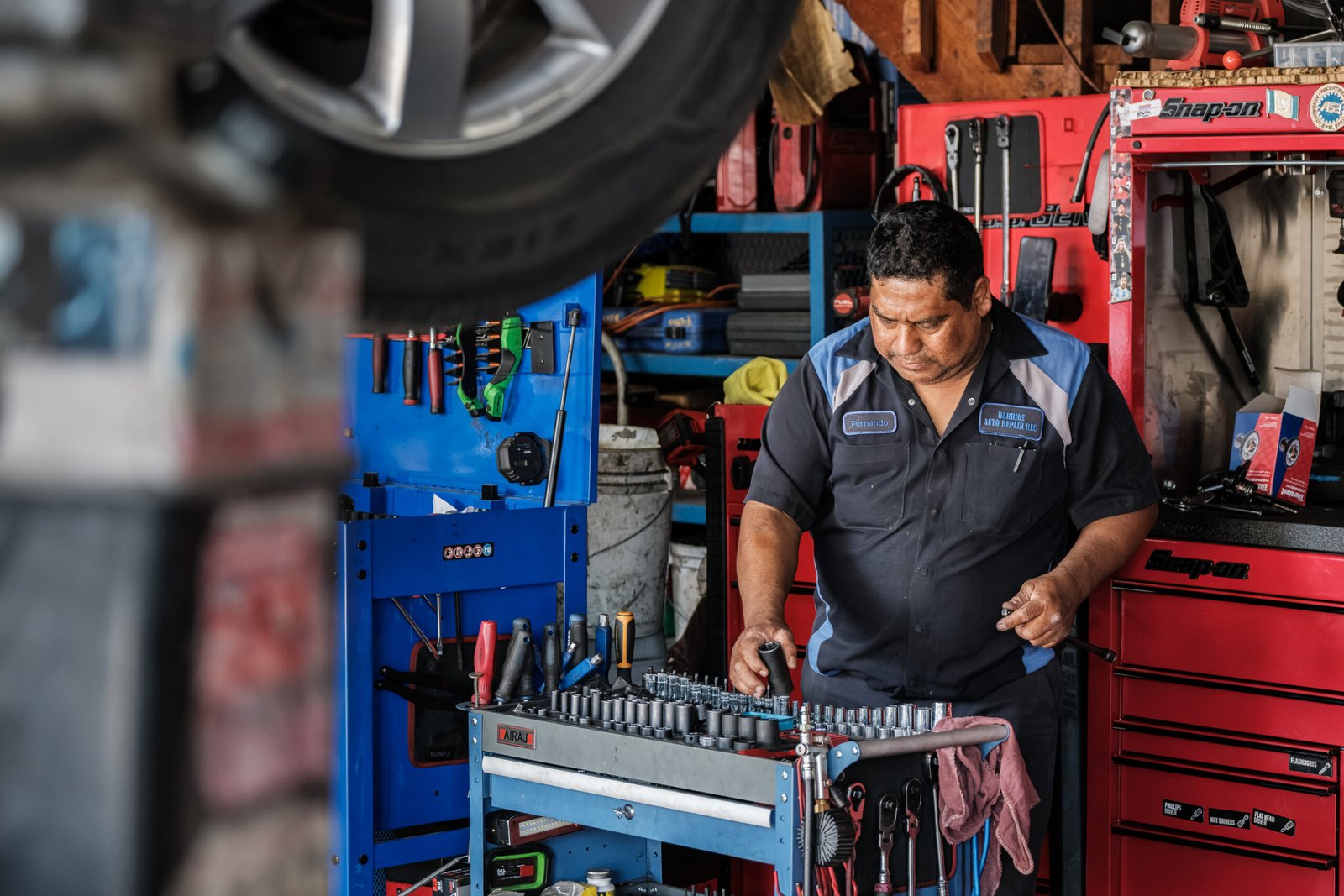 Barrios Auto Repair Van Nuys – mechanic at his tool chest in the service bay beneath a car raised on the lift.