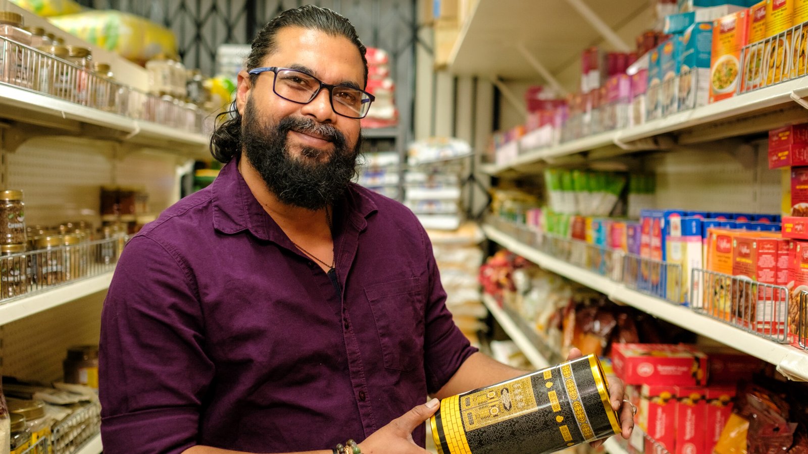 Bismillah Grocery & Meat Market – owner holding a packaged product in an aisle of halal groceries and spices.