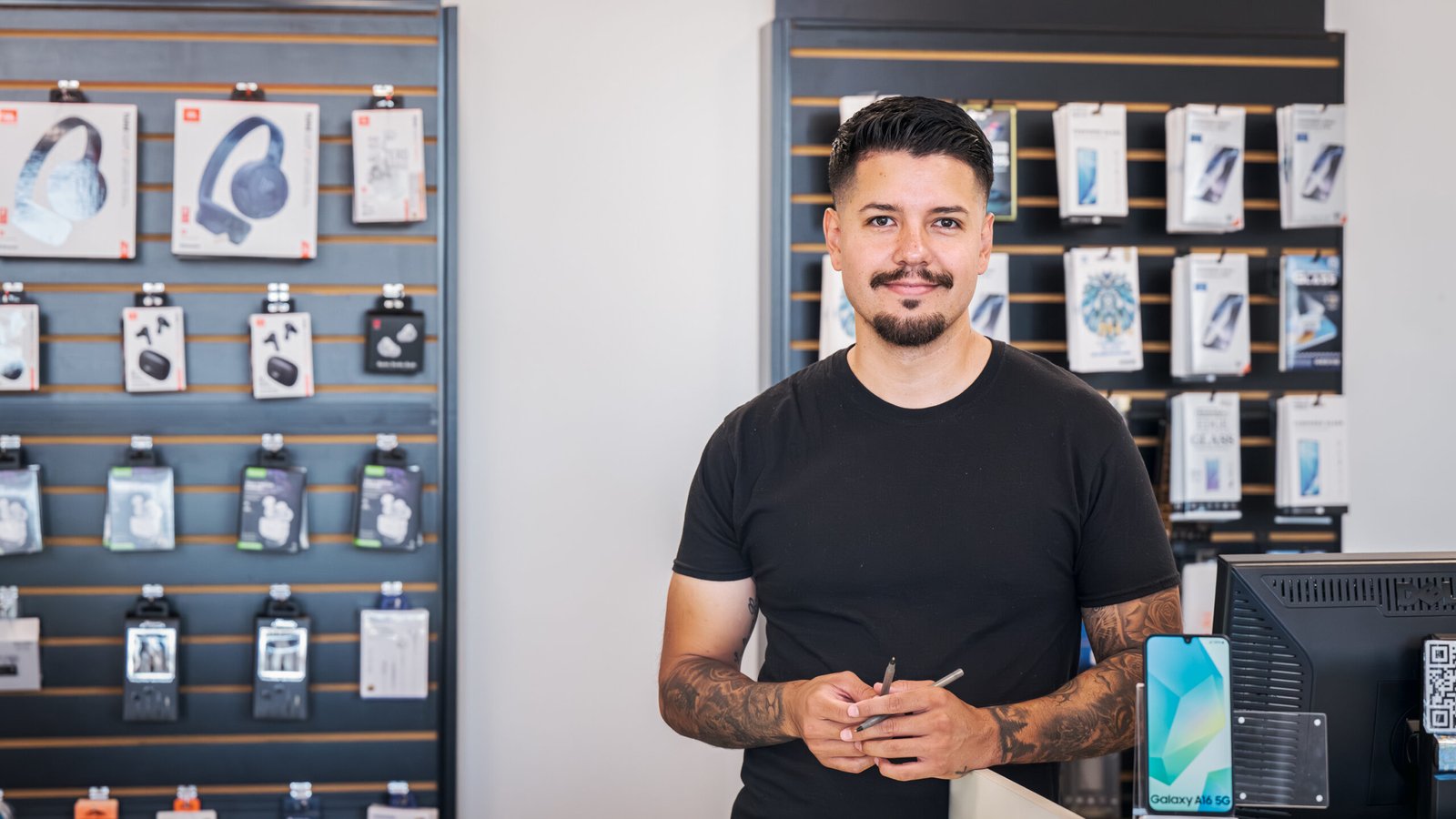 Boost Mobile Cell Phone Repair – store owner standing in front of a wall of phone cases, chargers and headphones.
