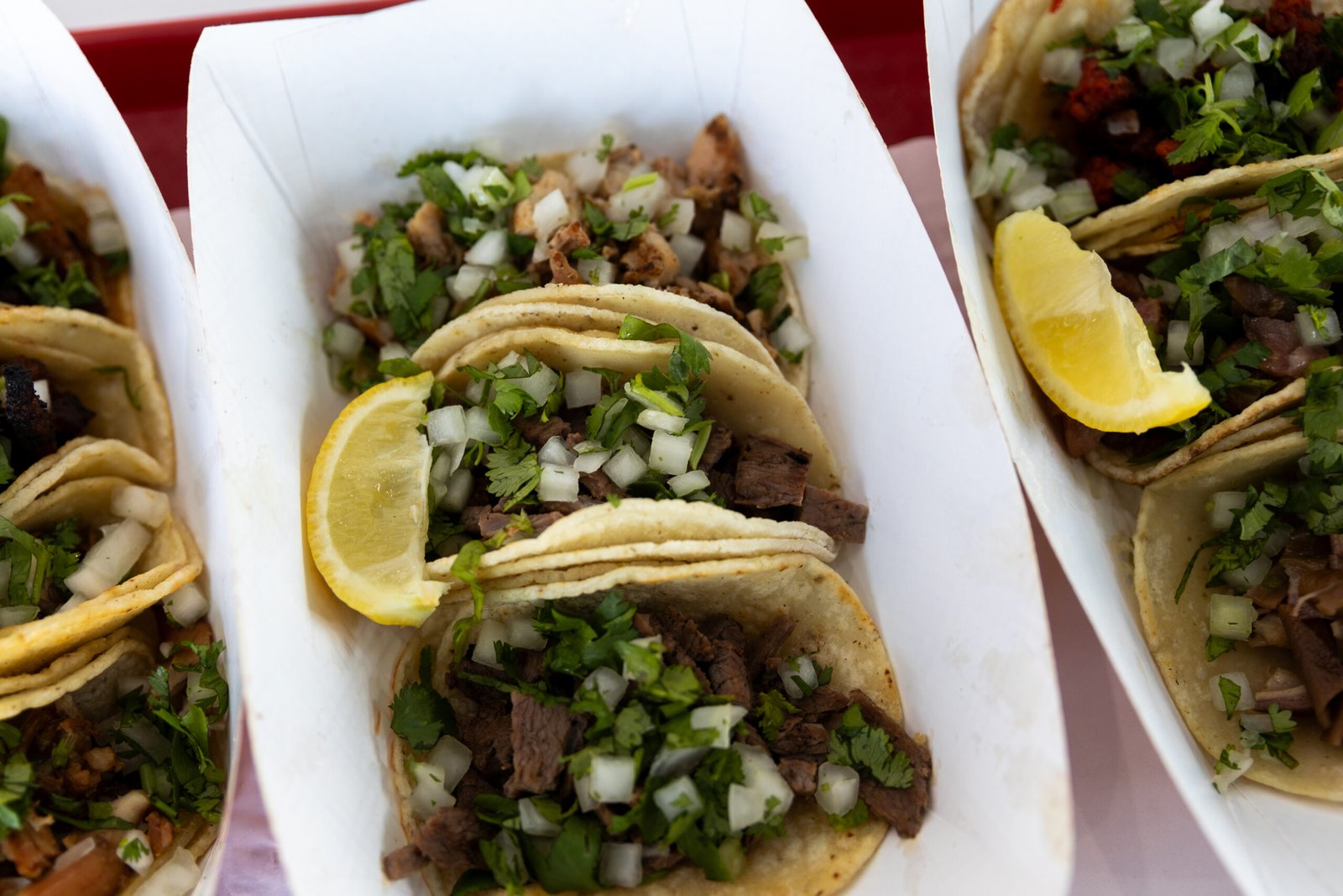El Gallo Giro – three street tacos topped with onion, cilantro and lime in a paper tray.