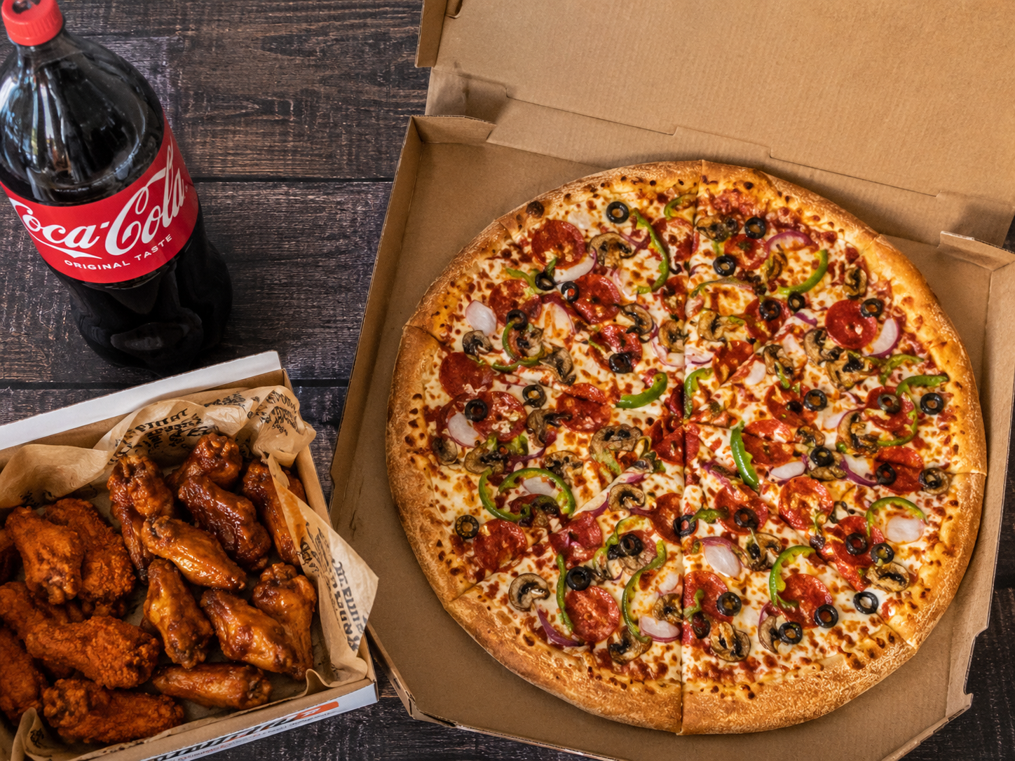 Next Level Pizza – large supreme pizza in an open box with a side of buffalo wings and a bottle of Coca-Cola.