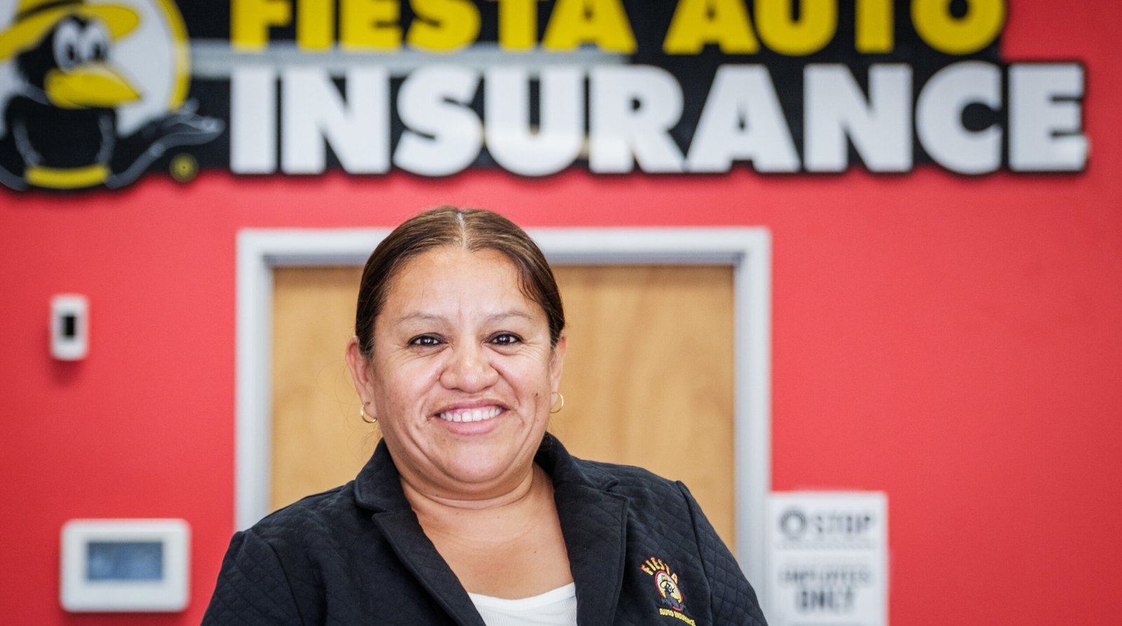 Fiesta Auto Insurance & Tax Service – agent smiling in front of the large red Fiesta Auto Insurance sign.