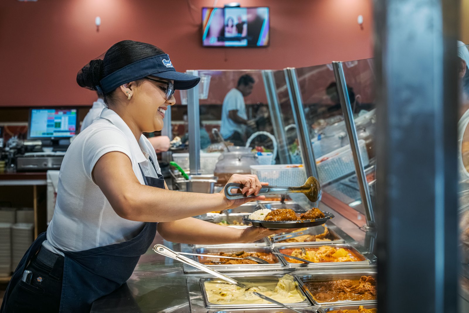 Guatemalteca Bakery – employee serving hot Guatemalan dishes from behind the steam table counter.