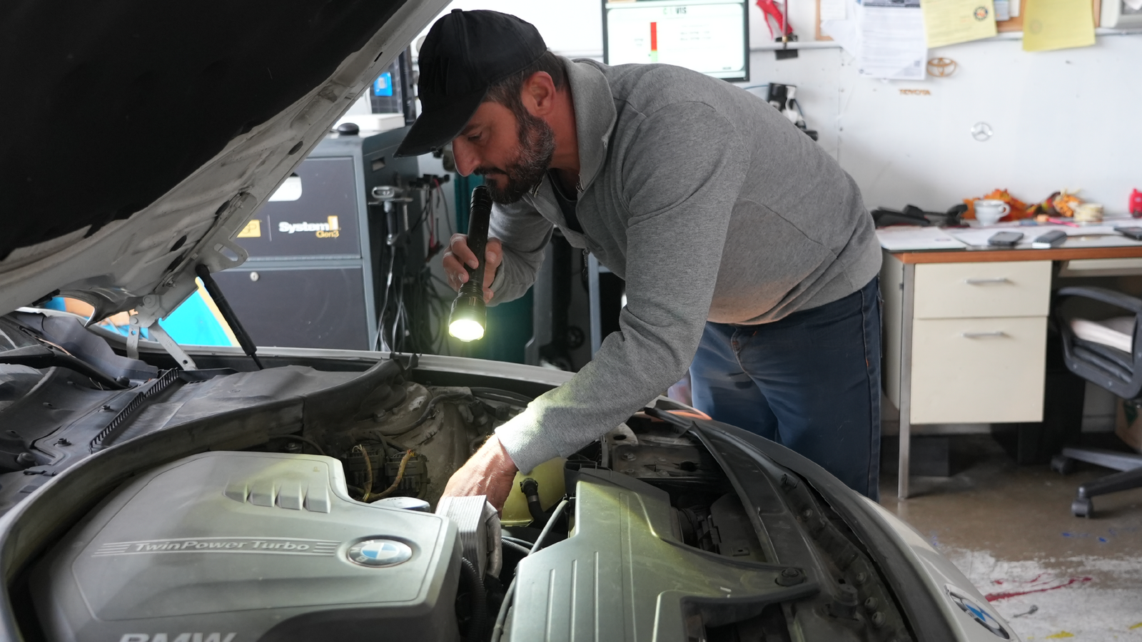 Van Nuys Smog – technician inspecting an engine under the hood with a flashlight during a smog check.